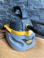 Front and side view of the Stinger wet/dry vacuum with attached hose on wooden surface and stone backdrop.
