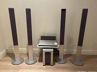 Front view of Sony home theater system components arranged in a corner, showing 4 tall tower speakers, central amplifier unit, center speaker and subwoofer.
