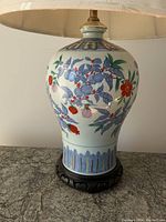 Front view of the vintage Asian porcelain table lamp with floral painted design and carved wood base.