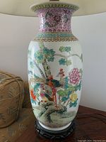Full view of the tall porcelain vase lamp with colorful birds and floral detailed painting on the body, sitting on a dark carved wooden base.