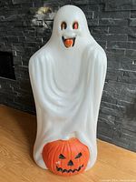 Full front view of vintage white ghost with orange pumpkin base against dark gray stone wall showing overall condition.