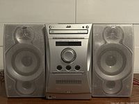 Front view of JVC FS-L30 compact stereo system with two speakers. Visible speaker cones and central unit with control dial and CD player.