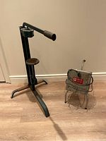 Photo of motorized wine filter with crank and stand next to a manual metal wine corker on a wood floor against a neutral wall.