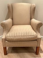Front view of classic wingback chair upholstered in beige striped fabric with wooden legs
