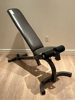 Side view of Bodysmith workout bench showing inclined backrest, padded seat, and black metal frame with curved base.