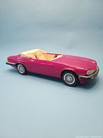 Side profile of the magenta Barbie Jaguar XJS toy car showing convertible beige interior and detailed wheels.