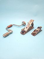 Three antique woodworking tools on a light blue background: large and small Stanley hand planers and a hand drill.