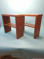 Front and angled view of two teak wood custom side tables with an open shelf between the legs.