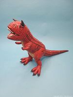 Full side view of red Carnotaurus dinosaur figure showing body length, posture, and details of legs and feet with wire posability.