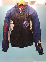 Front view of the Giants varsity jacket with black leather body and blue sleeves. 'GIANTS' text in red on right sleeve and helmet patch on left chest.