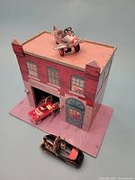 Front view of the firehouse playset with the airplane pedal car on top and the fire truck pedal car inside the firehouse garage.