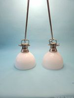 Pair of pendant lights with polished nickel finish and white opaque glass shades shown with rods and hanging hardware, front view