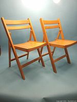 Pair of Mid-Century Modern folding wooden chairs, viewed at an angle showing the front and side profile.