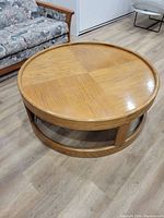 Side angled view of a circular mid century modern oak coffee table with parquet top, showing its base and rim details.