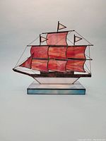 Front view of the stained glass tallship sculpture showing red sails and blue-white base