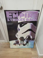 Front view of the Star Wars Empire Strikes Back placard depicting a Stormtrooper helmet with AT-AT walkers advancing, showcasing the title text in purple.