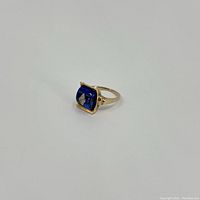 Angle view of the 10k yellow gold ring showing blue glass stone with diamond centerpiece.