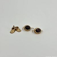 Pair of 14k gold baby shoe charm and a pair of 14k gold earrings with dark red faceted stones.