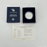 Blue United States Mint box with silver coin in protective capsule inside, along with coin specifications card.
