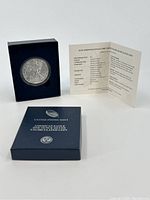 2015 American Eagle silver coin in blue display box with certificate of authenticity open behind it.