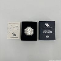 Photo of the 2017 American Eagle silver coin in its black velvet display box, flanked by the certificate of authenticity and outer box.