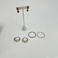 Overall view of all three pairs of earrings together, showing two pairs of silver hoops and one pair of heart-shaped dangle earrings.