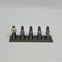 Five rings displayed on a black ring stand, showing different designs and stones