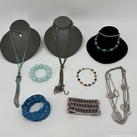 Group of 8 costume jewelry pieces including various necklaces and bracelets on display stands and flat on table
