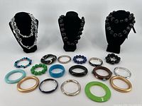 Full view of three necklace busts with large bead necklaces, along with various colored and styled bracelets laid in front on table.