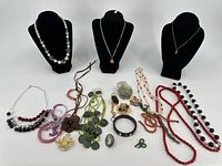 Wide photo of group of costume jewelry including various necklaces and bracelets displayed on black busts and on table