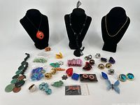 Wide view of entire costume jewelry collection with necklaces on busts, assorted rings, earrings, brooches laid out on flat surface.