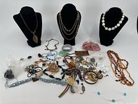 Group of assorted costume jewelry items including necklaces on black busts and various loose bracelets, rings, pendants, and chains spread on a white surface.