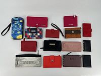 Overview of 14 assorted ladies wallets in various colors and styles laid flat on white surface.