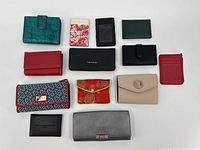 Photo displaying 12 assorted ladies wallets in various styles and colors arranged on a white surface.