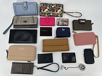 Group of sixteen assorted ladies wallets and small accessories laid out on a white surface showing various colors, sizes, and designs.