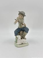 Front view of Lladro porcelain figurine showing seated boy playing flute with lamb at base.