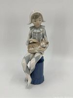 Front view of porcelain figure showing seated child in blue and white clown outfit holding a cat while sitting on blue stool.