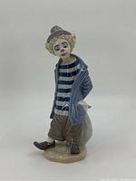 Front view of porcelain clown figurine showing blue striped shirt, open coat, curly hair, and facial makeup.