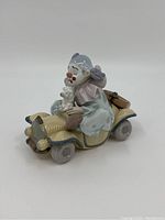 Side view of porcelain Lladro clown figure seated in vintage car holding small dog.