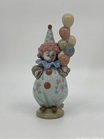 Front view of glossy porcelain clown figurine holding balloons with detailed costume and facial paint