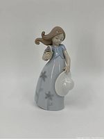 Front view of the Lladro porcelain figurine showing the girl holding a flowerpot and hat, wearing a light blue dress with flower details.