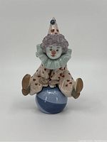 Front view of Lladro porcelain clown figurine seated on blue and white ball, showing facial details, ruffled collar, and heart decorations on clown outfit.