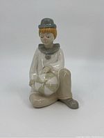 Front left angle view of porcelain clown figure sitting holding a ball.