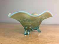 Side view of antique green carnival glass dish showing ruffled edge and textured pattern on the surface with three small legs.