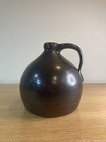 Front angle view of dark brown antique stoneware whisky jug with handle