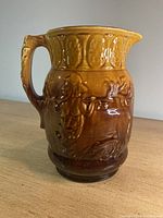 Front and side angle view of the brown glazed ceramic pitcher showing detailed centaur design and handle shape.