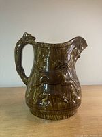 Front view of brown Bennington-Rockingham ceramic pitcher with sculpted hound handle and hunt scene