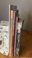 Five art and craft books standing upright on a surface next to a ceramic sculpture. Titles include Bonsai with American Trees, How to Make Modern Jewelry, Drawing, Dorothy Heizer and Her Dolls, Pottery and Porcelain.