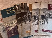 Photo showing six war pamphlets and booklets with covers depicting marines and naval scenes in color and black and white.
