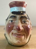 Front view of grotesque face jug showing detailed facial features and spout with chip.